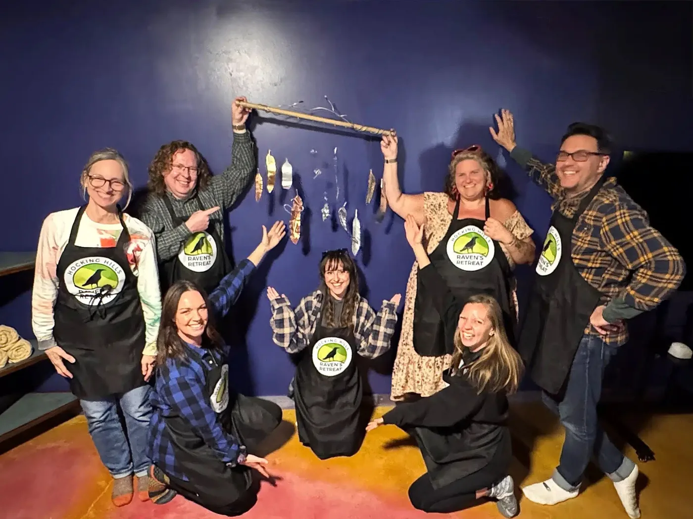 A workshop group in Raven's Retreat aprons celebrating the collaborative hanging sculpture they built together