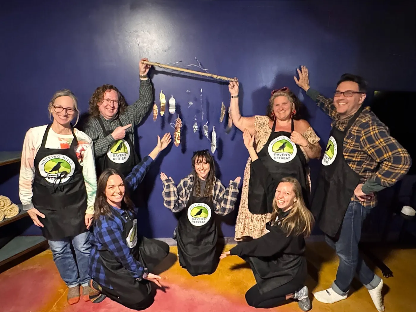 A corporate team in Raven's Retreat aprons showing off the hanging sculpture they made together