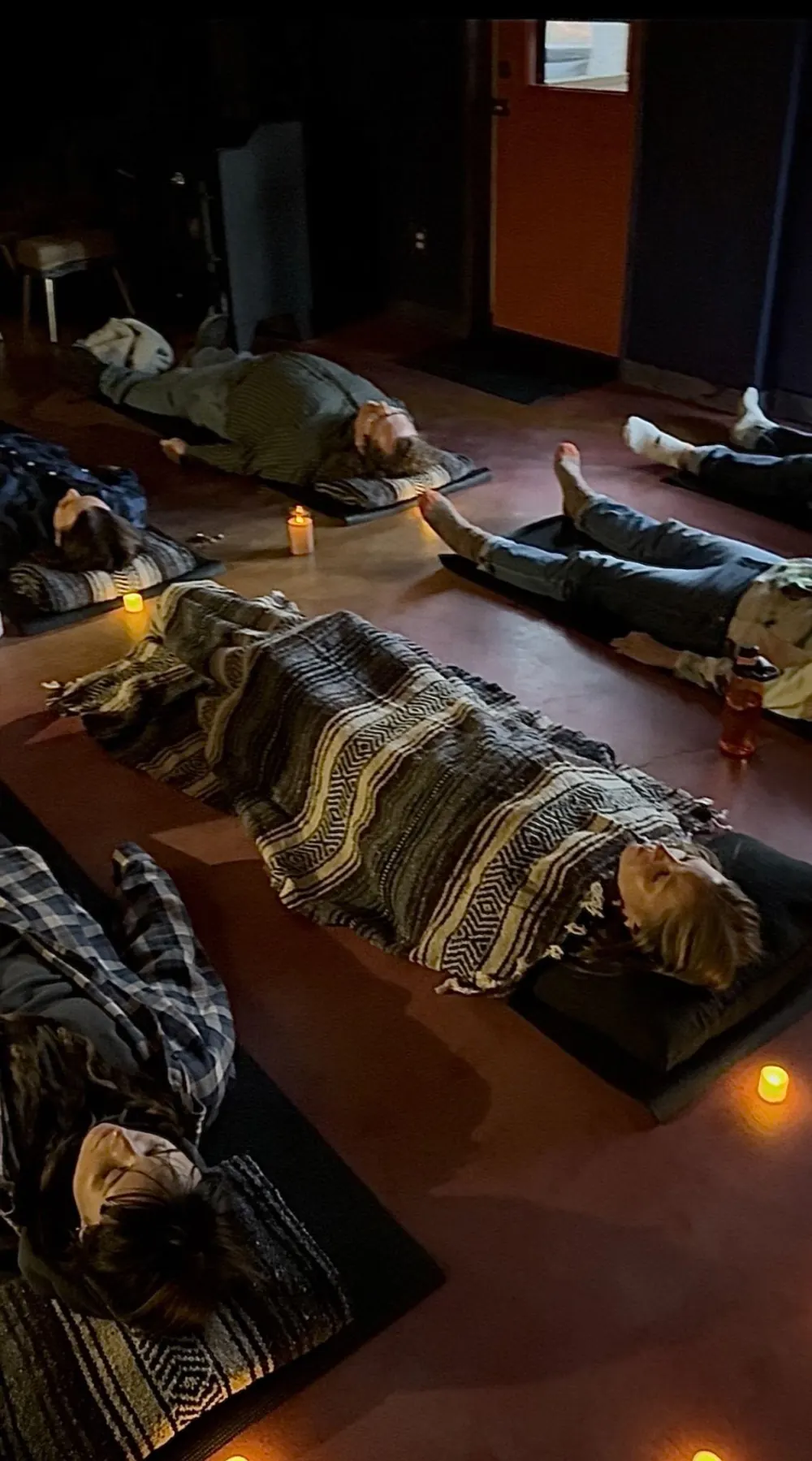A team lying on mats under blankets during a candlelit group somatic breathwork session