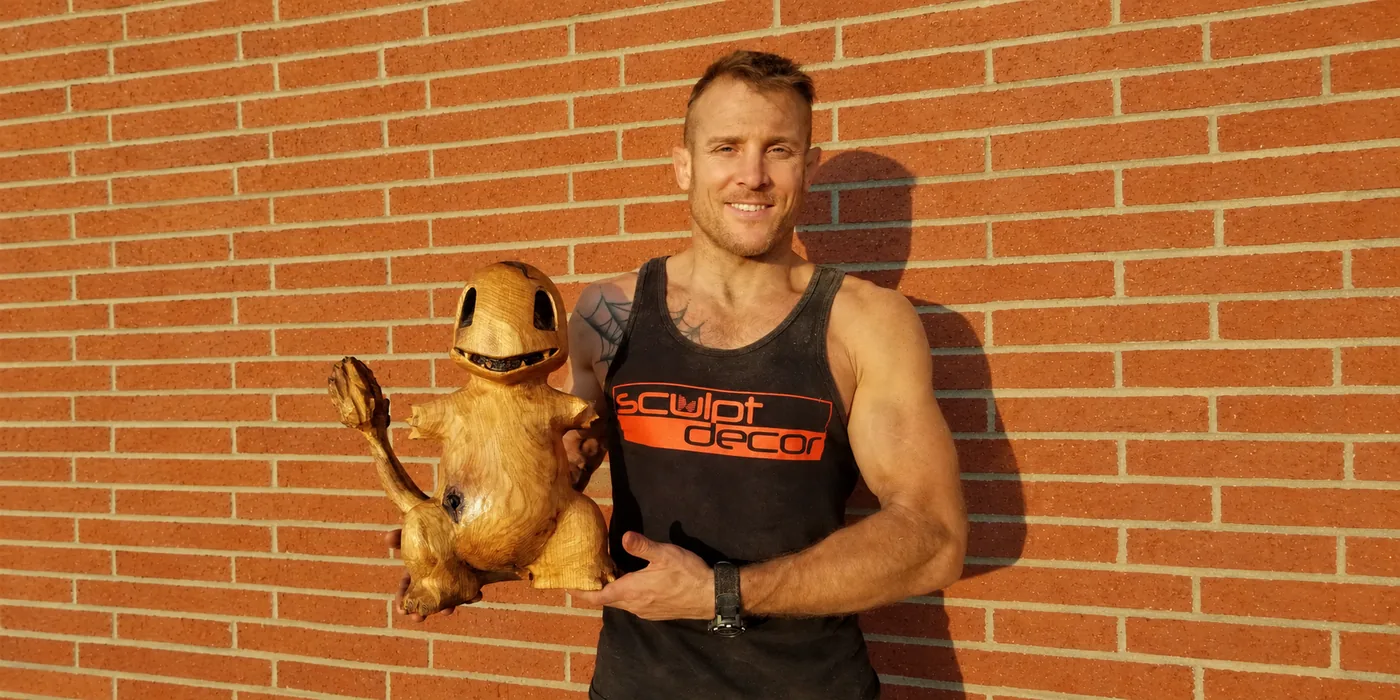 Master sculptor Dustin Weatherby holding a hand-carved wood dragon sculpture at Raven's Retreat Hocking Hills