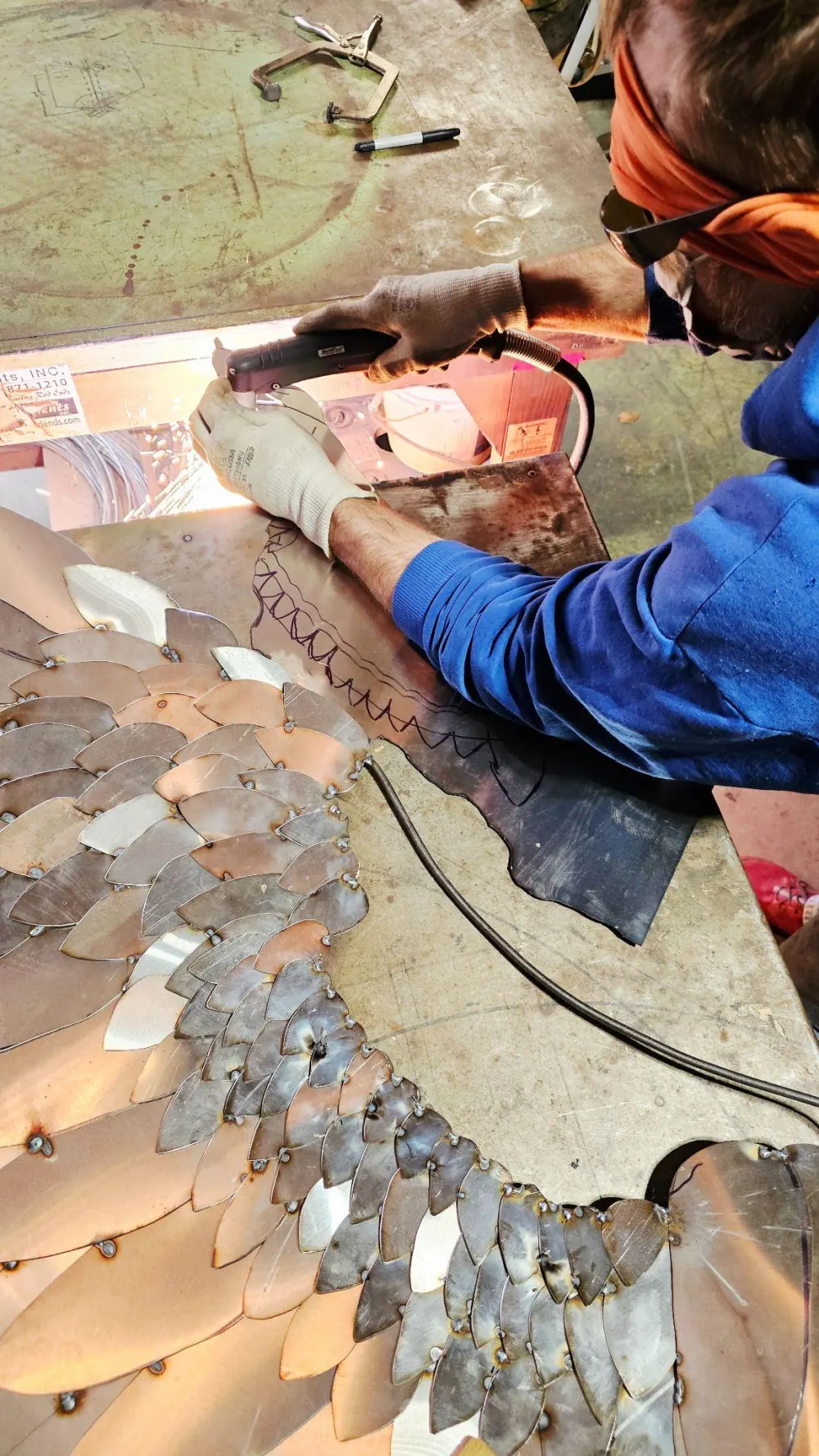 Dustin Weatherby plasma-cutting the metal feathers of a wing sculpture in the SculptDecor studio