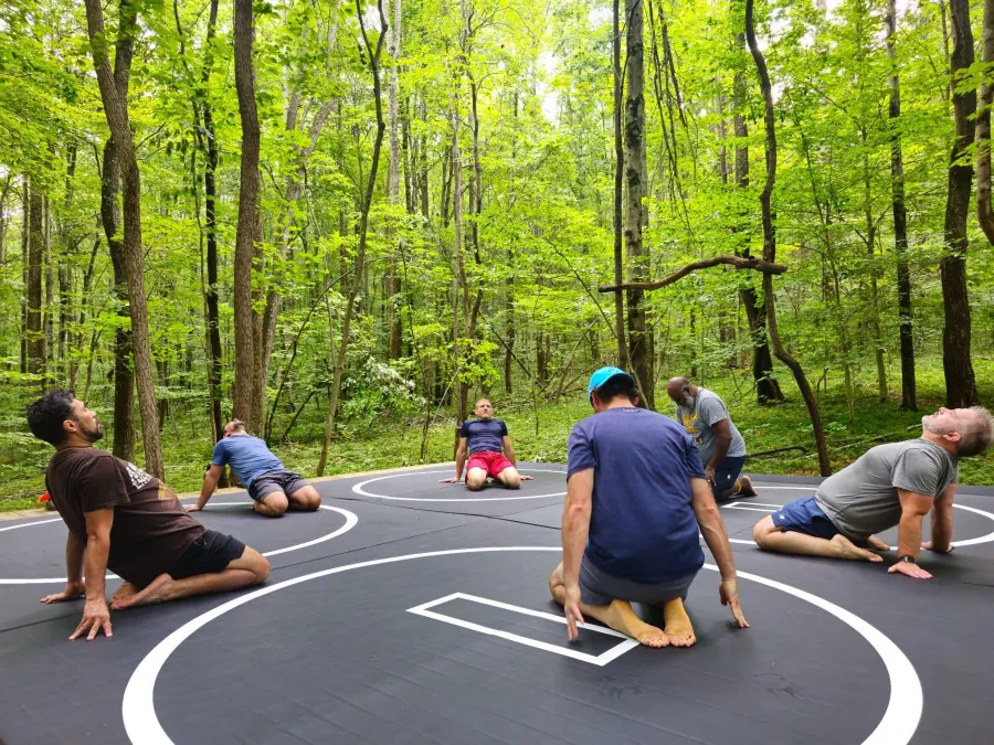 Men's retreat guests stretching together on the outdoor combat training mats in the forest at Raven's Retreat Hocking Hills