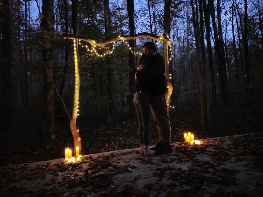 A couple at their candlelit ceremony arch in the forest at Raven's Retreat