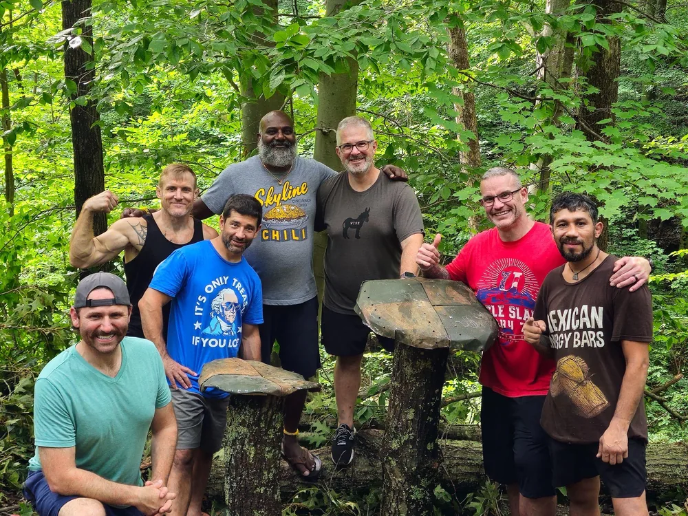 Men's retreat group gathered in the forest beside a trail sculpture at Raven's Retreat Hocking Hills