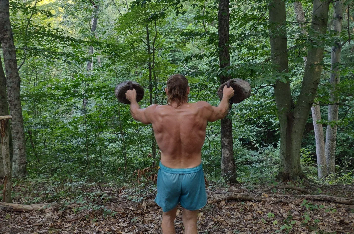 Guest holding two log weights out to the sides on the wellness trail at Raven’s Retreat Hocking Hills