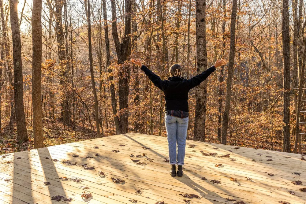 A guest with arms raised on the forest platform in autumn, a typical Hocking Hills painting subject
