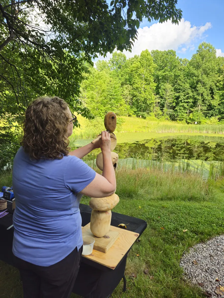 Guest shaping a wooden sculpture at a workbench overlooking the pond during a sculpting workshop