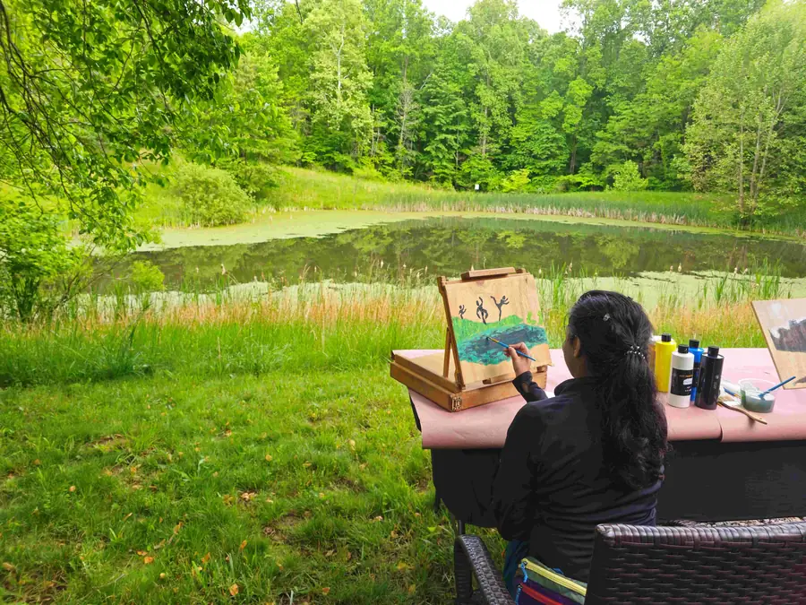 Solo retreat guest painting at an easel overlooking the pond at Raven's Retreat Hocking Hills