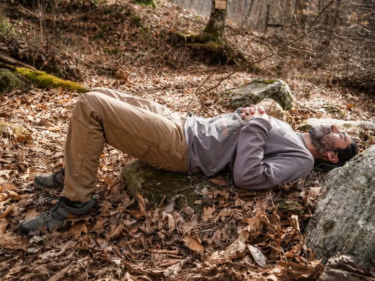 A solo guest lying back on a moss-covered rock among the fallen leaves on the preserve at Raven's Retreat