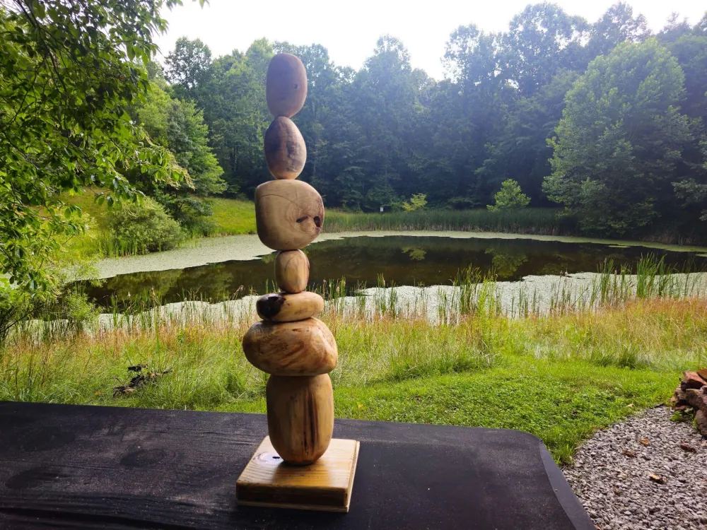 A stacked wood sculpture made in a sculpting workshop, set beside the pond at Raven's Retreat