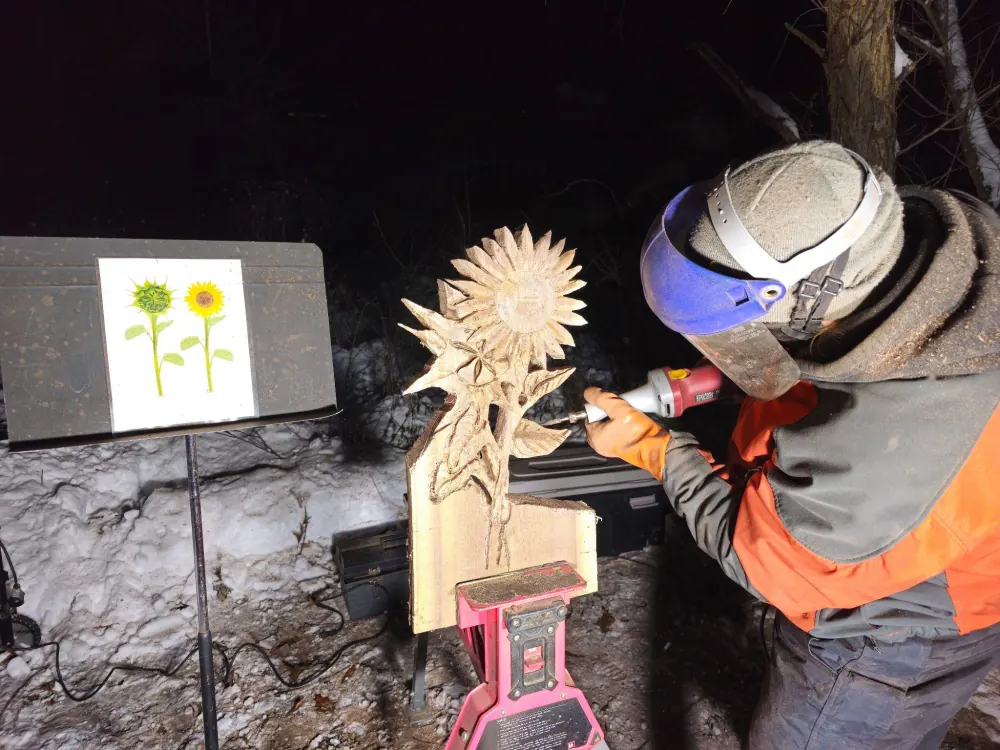 Dustin Weatherby carving a sunflower sculpture at night during a live sculpture performance
