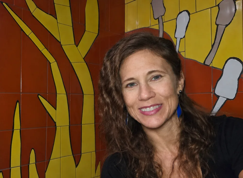 Raven Morgan, lifestyle coach at Raven’s Retreat, smiling in front of a colorful tile mural